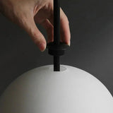 A hand holding one of the white glass spheres beside its black fitting