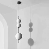 Three white spheres threaded on a black rod against a pale plaster wall