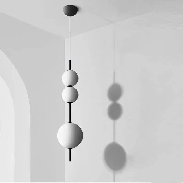 Three white spheres threaded on a black rod against a pale plaster wall