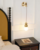 The gold ball light hanging beside a bed above a nightstand with a print