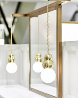 Three ball lights at different heights beside a brass framed mirror