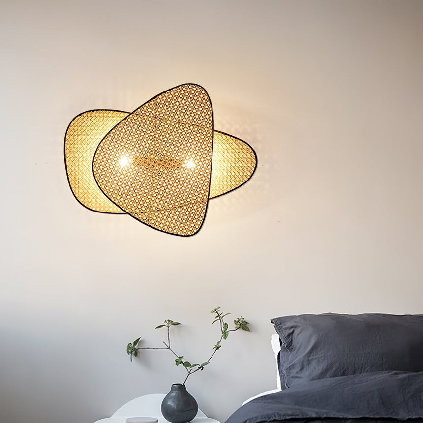 The cane sconce lit above a bed with dark linens and a small side table