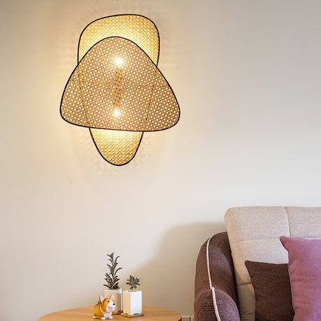 The cane sconce lit above a pink sofa and a small side table with a plant
