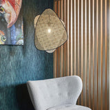 The cane sconce on a dark wall above a white wool chair beside wood slats
