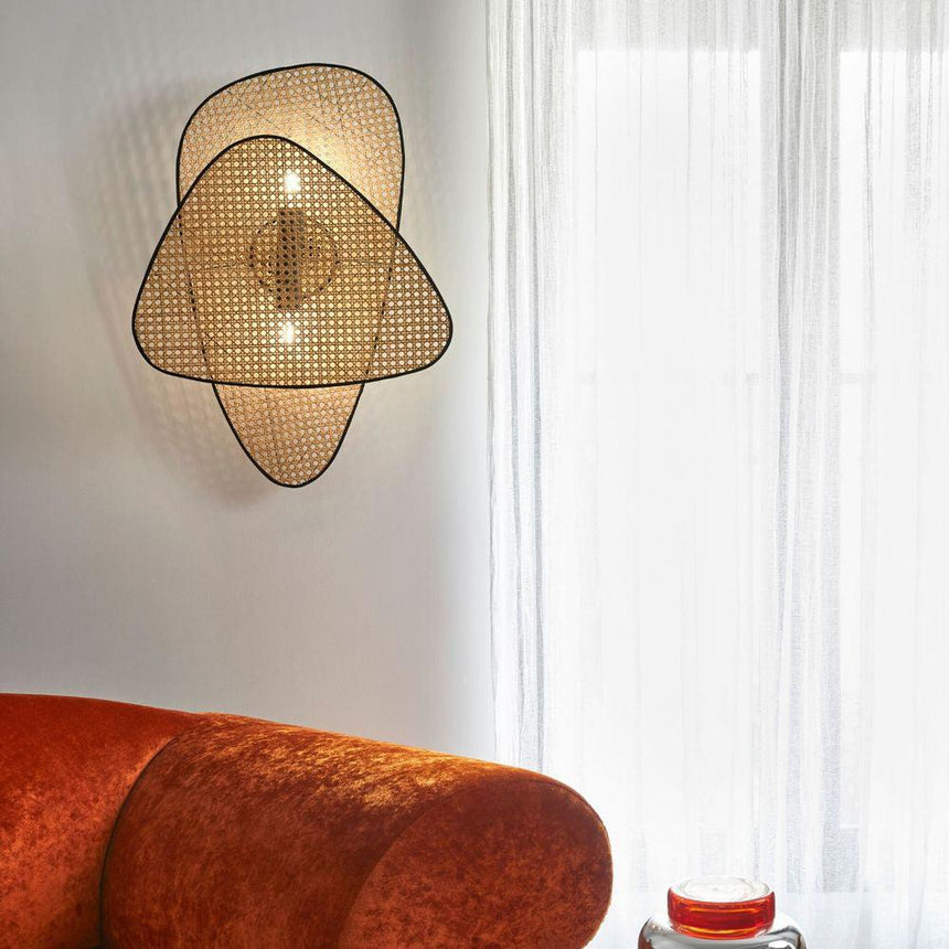 The cane sconce lit on a white wall above a rust velvet sofa by a curtain