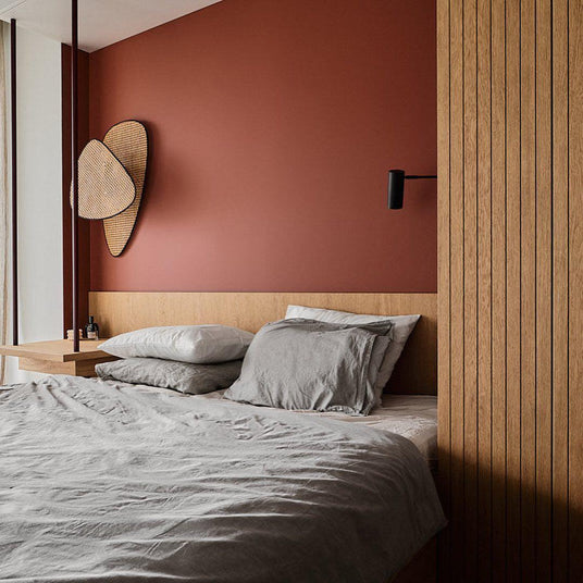 Cane sconce on a terracotta bedroom wall above a bed and slatted wood panels