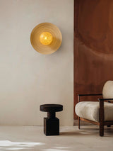 Sconce lit on a warm wall beside a black stool and a pale armchair