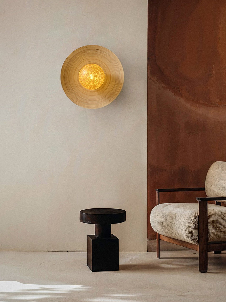Sconce lit on a warm wall beside a black stool and a pale armchair