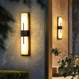 Two bar lights lit on stone walls beside a doorway, a small tree in front