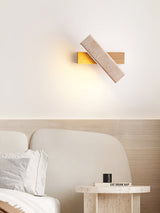 Sconce lit above a bed with pale cushions and a round stone side table