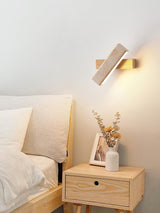 Sconce lit beside a bed above a nightstand holding dried flowers