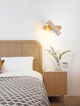 Sconce lit above a cane headboard beside a nightstand with a small plant
