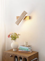 Sconce lit beside a wood nightstand holding flowers, a candle and books