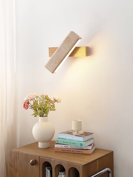 Sconce lit beside a wood nightstand holding flowers, a candle and books