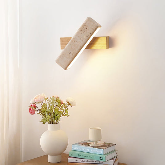 Sconce lit above a nightstand with flowers in a white vase and books