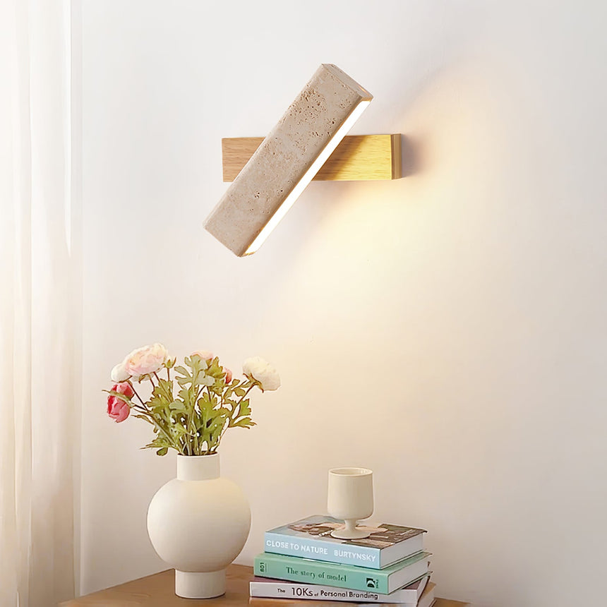 Sconce lit above a nightstand with flowers in a white vase and books
