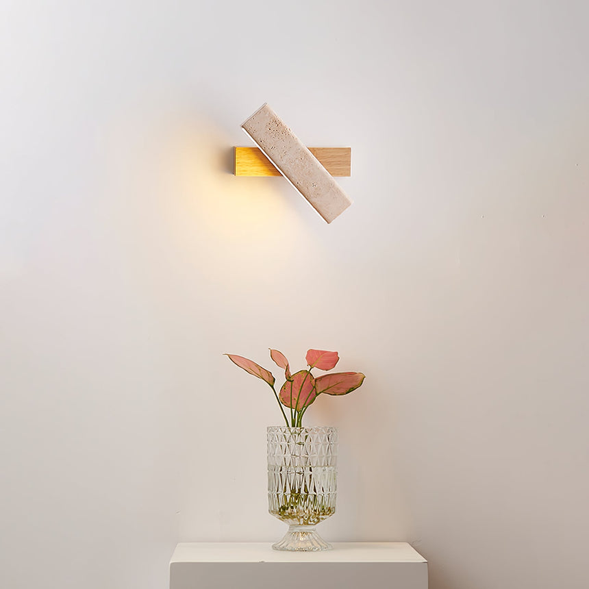 Sconce lit above a nightstand with tulips in a glass vase beside a bed