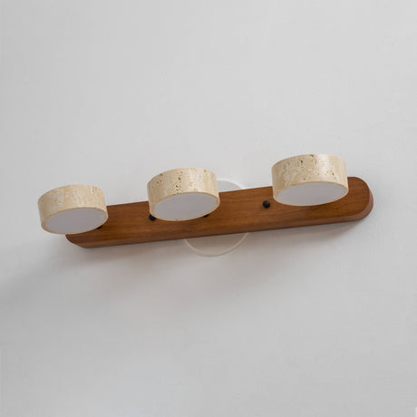 Three travertine discs lit along a light wood bar, seen from an angle