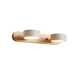 Two travertine discs lit on a light wood bar against a plain wall