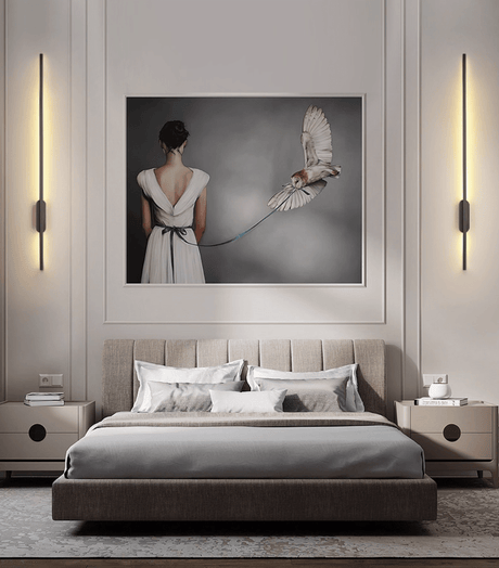 A lit pair either side of a framed artwork above a bed with gray bedding