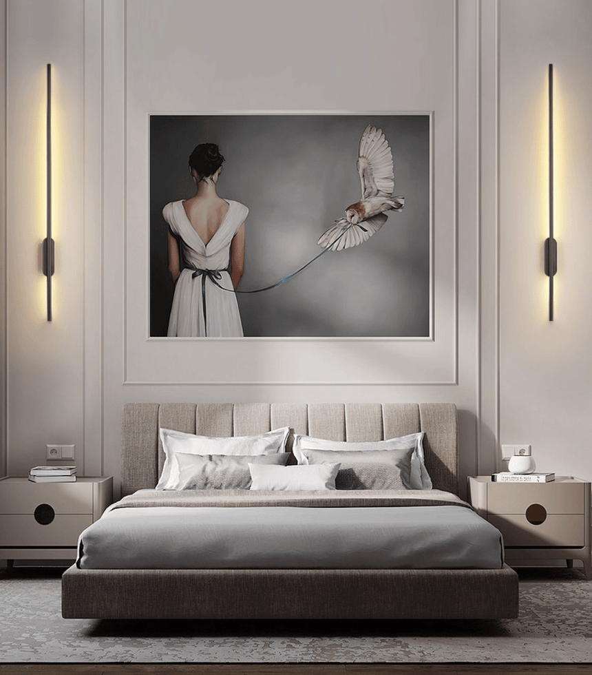 A lit pair either side of a framed artwork above a bed with gray bedding