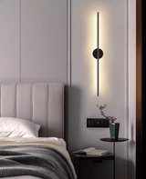 Lit beside a bed with a padded headboard, a small plant on the nightstand