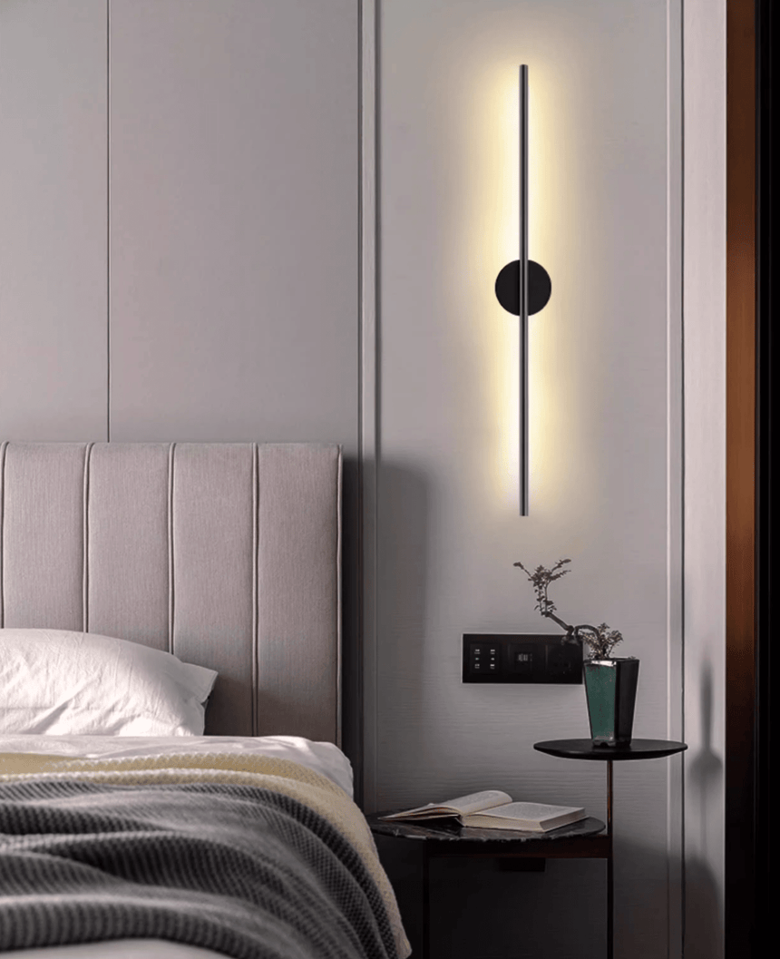 Lit beside a bed with a padded headboard, a small plant on the nightstand