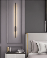 Lit beside a padded headboard above a nightstand with books stacked on it