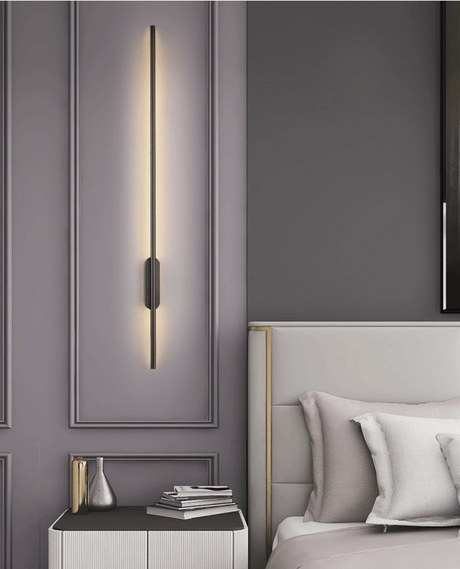 Lit beside a padded headboard above a nightstand with books stacked on it