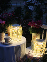 Two lit on a cloth covered table beside a cup and potted flowers