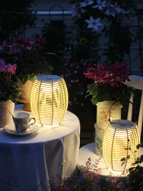 Two lit on a cloth covered table beside a cup and potted flowers