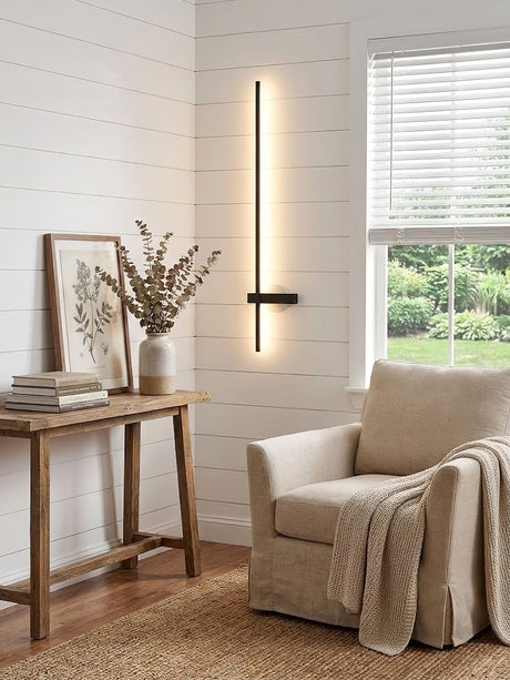 Lit on a plank wall beside a pale armchair and a narrow console table
