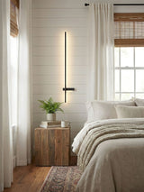 Lit in a bedroom beside a window, a timber nightstand and a small plant