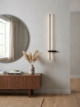 Lit beside a round mirror above a timber sideboard with a vase of grasses
