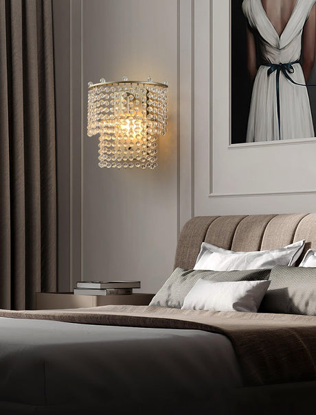 The beaded sconce lit above a bed with a tufted headboard and gray linens