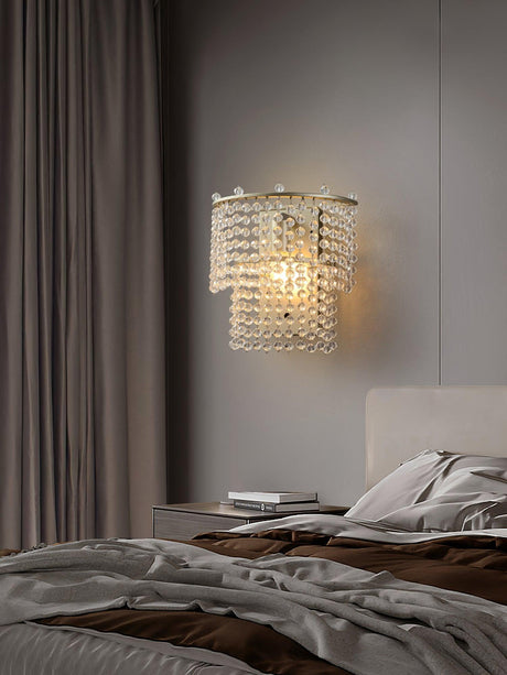 The beaded sconce lit above a bed with rumpled linens and a curtain