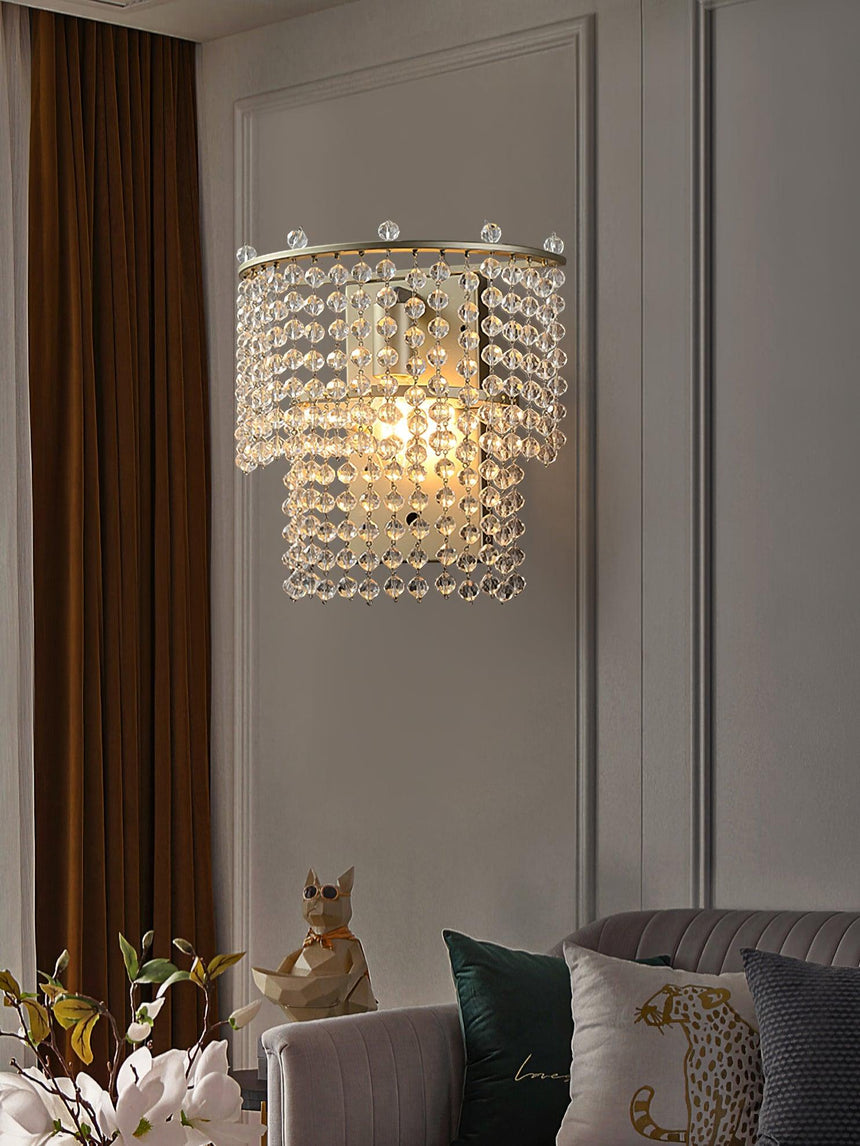 The beaded sconce lit above an armchair with a cushion beside long curtains