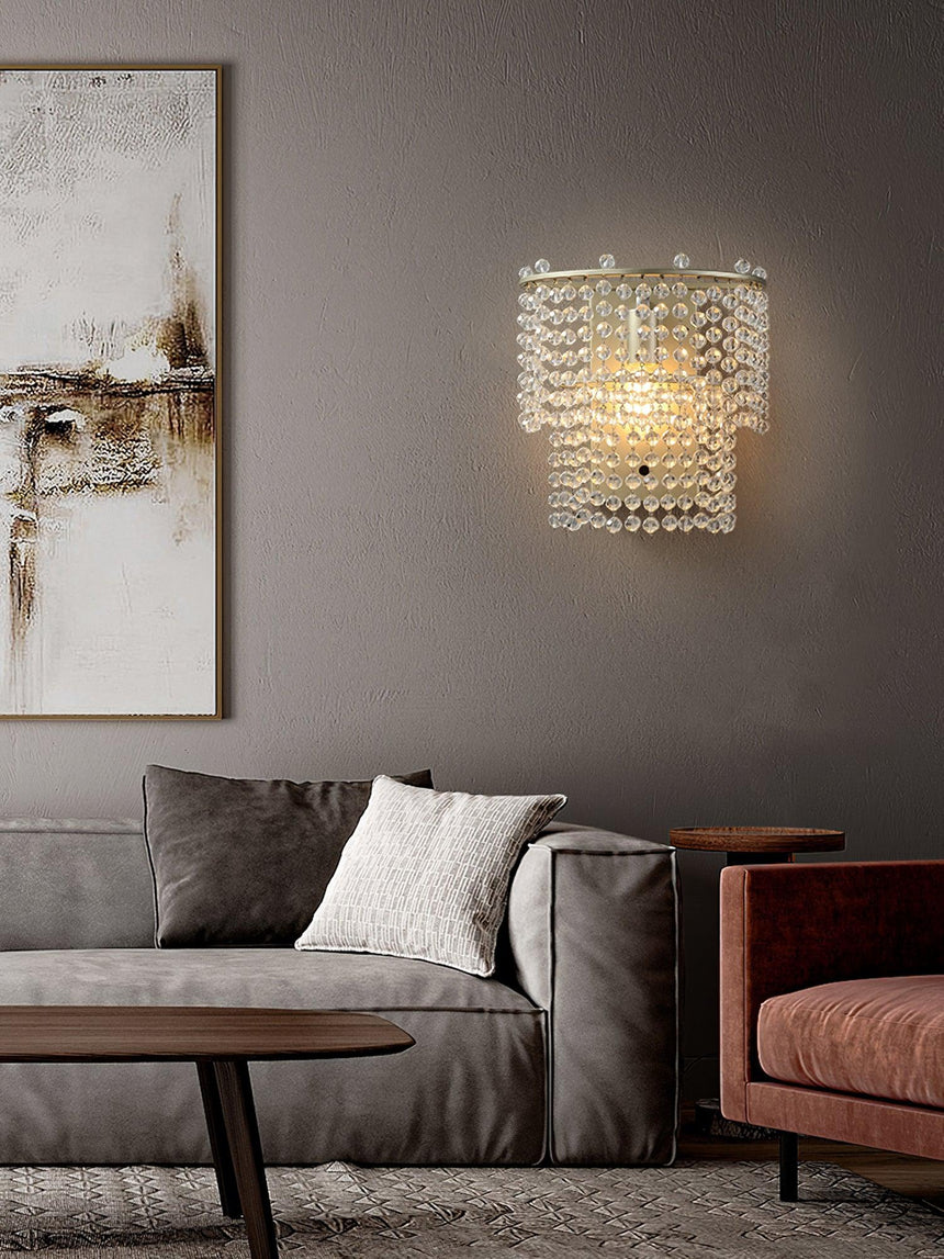 The beaded sconce lit above a gray sofa beside an abstract painting