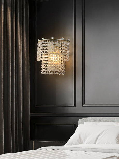 The beaded sconce on a dark paneled wall above a bed with white linens