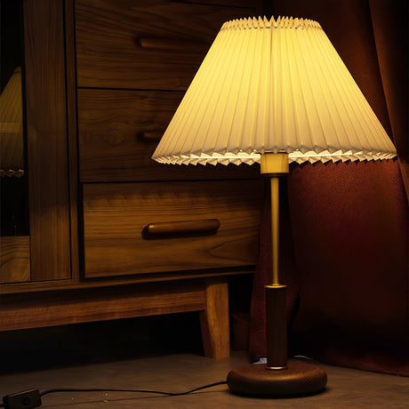 Pleated shade bedside lamp lit on a dark wooden dresser at night