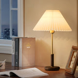 Pleated shade lamp lit on a desk beside books at a city window