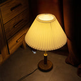 Pleated shade bedside lamp lit close up on a dark wooden dresser