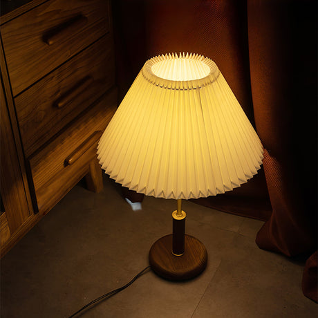 Pleated shade bedside lamp lit close up on a dark wooden dresser