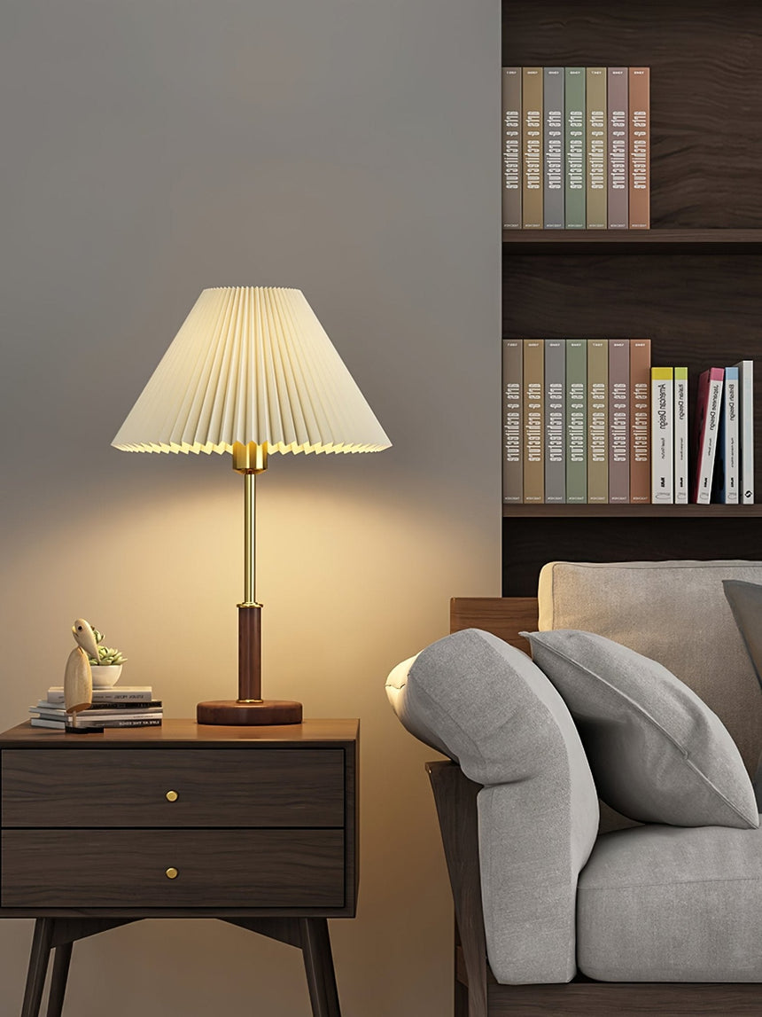 Pleated shade bedside lamp lit on a wooden nightstand beside a sofa
