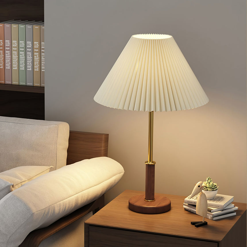 Pleated shade lamp lit on a side table beside a pale sofa and a tray