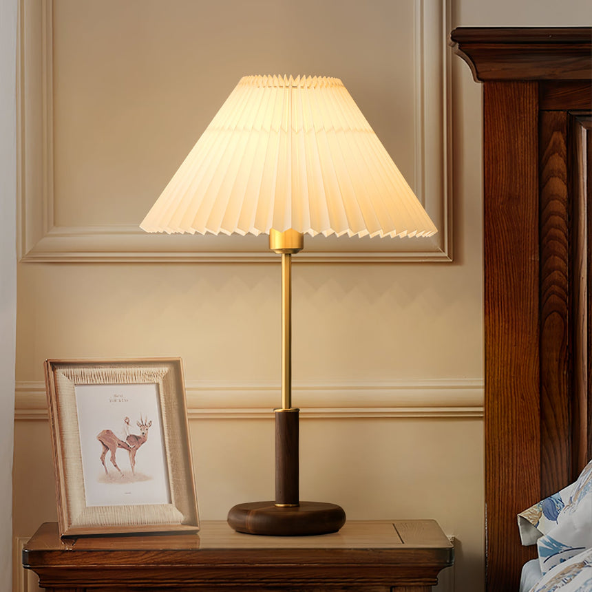 Pleated shade bedside lamp lit on a nightstand beside a framed print
