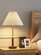 Pleated shade bedside lamp lit beside photo frames and a pillow