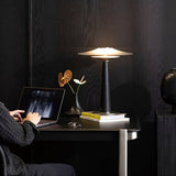 Bedroom table lamp lit at a workspace beside a laptop and flowers