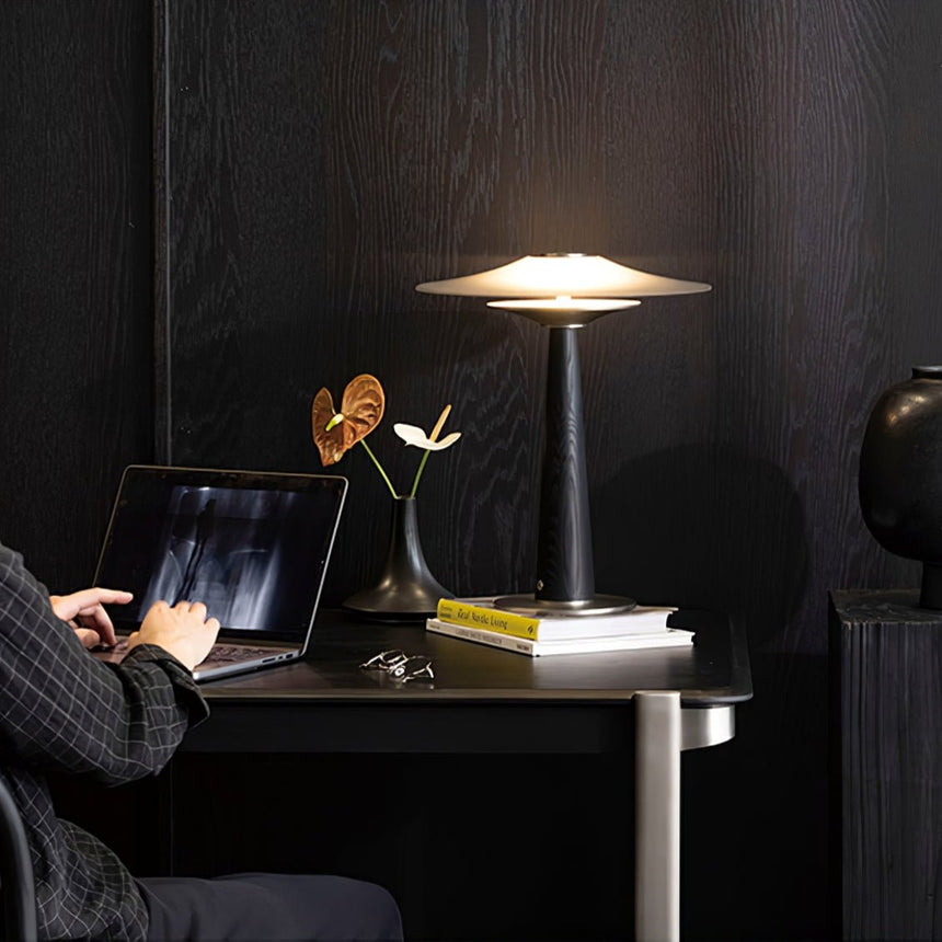 Bedroom table lamp lit at a workspace beside a laptop and flowers
