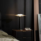 Bedroom table lamp lit on a nightstand beside rumpled bedding